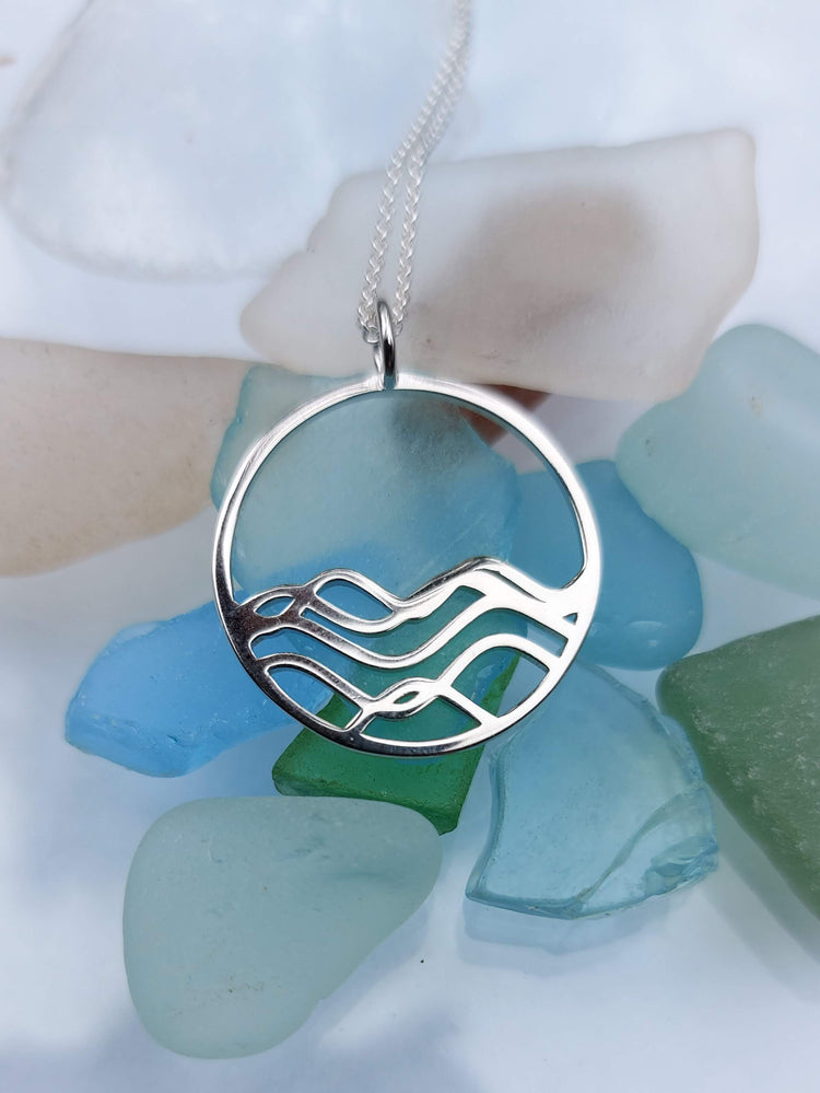 Sterling Silver Ocean wave circle pendant necklace on a bed of beach glass