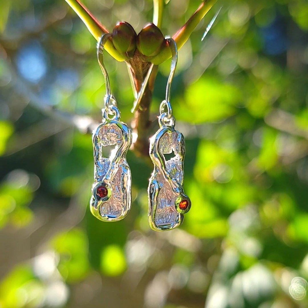 organic textured garnet and silver dangle earrings lit by the sun in front of greenery