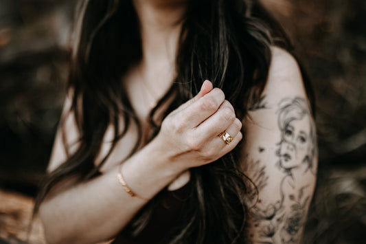model with tattoo wearing gold Natural textured gold ring with peridot stone
