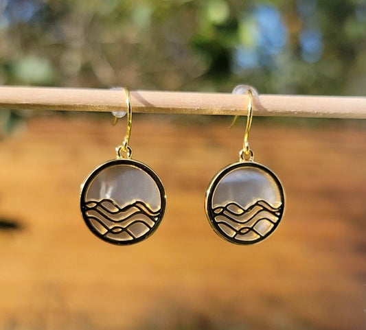 gold mother of pearl circle earrings. ocean wave dangle earrings on dowel with wood and green background