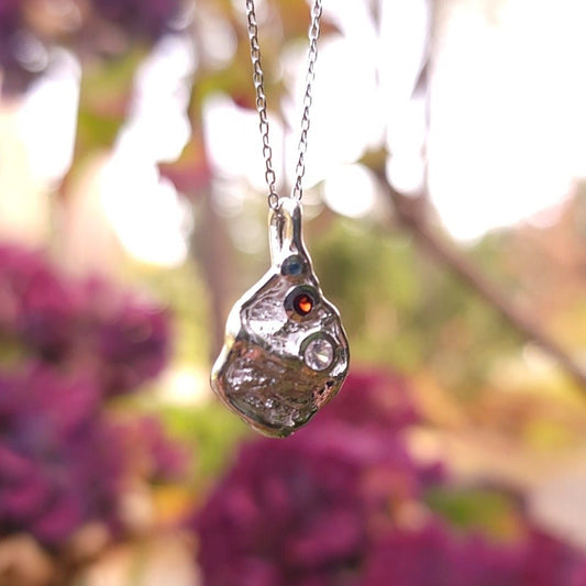close up of one of a kind silver pendant necklace with garnet, zircon and blue topaz gemstones