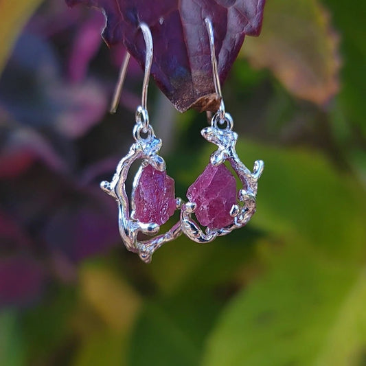 Raw pink tourmaline silver dangle earrings, with a branch and leaf setting, hanging from a leaf.
