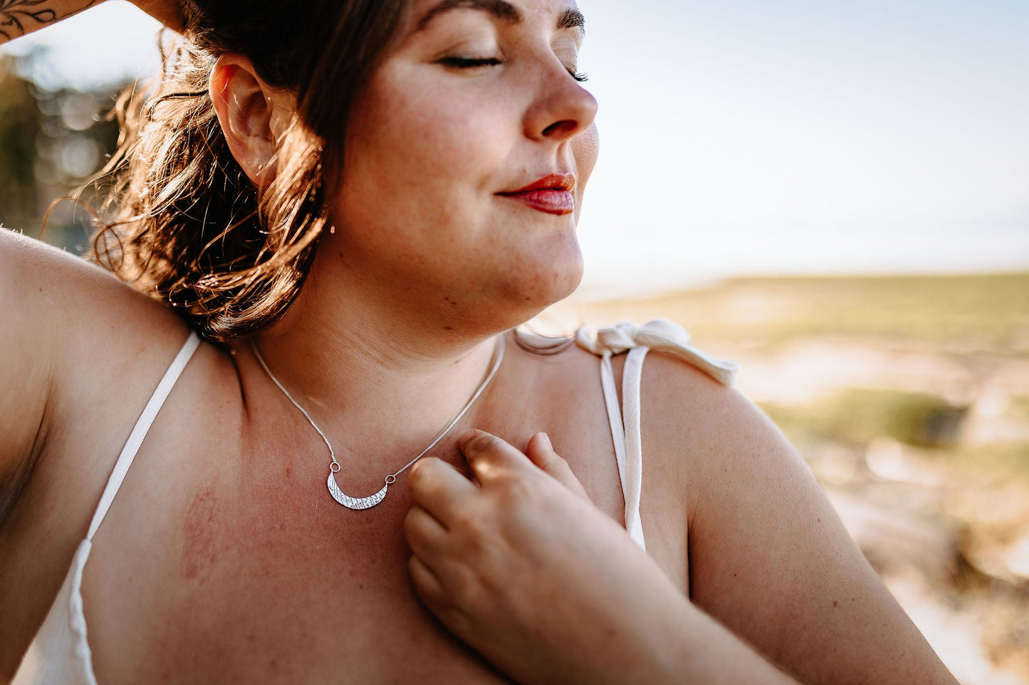 model wearing silver hoop marina earrings in sterling silver in sunshine under a tree 2