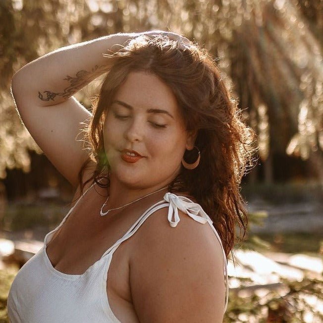 model wearing silver hoop marina earrings in sterling silver in sunshine under a tree.
