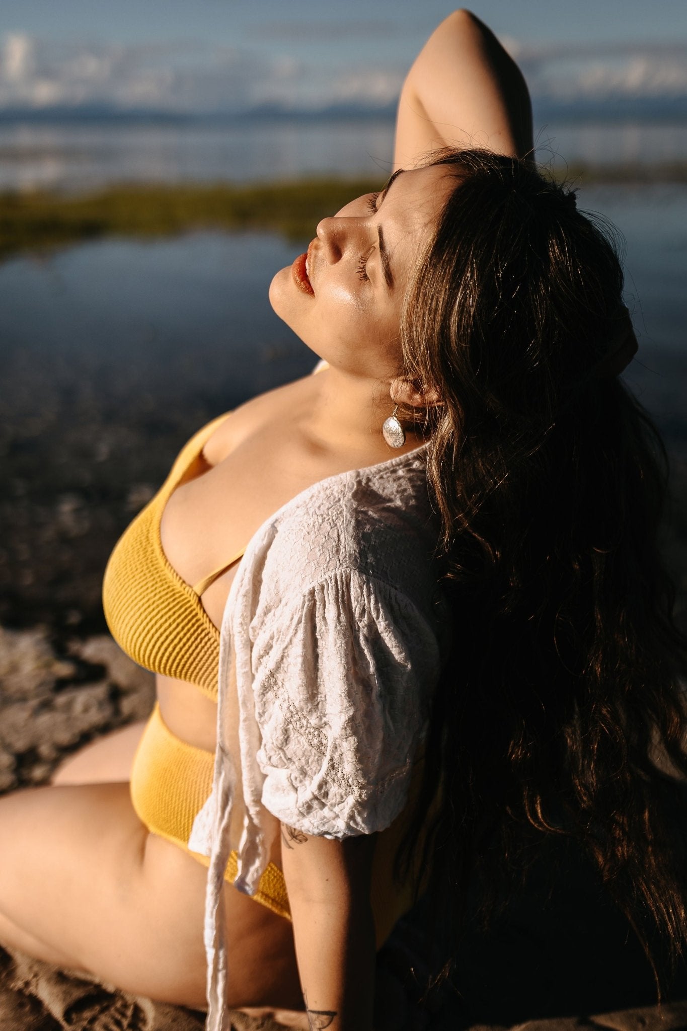 side view- model wearing silver Talia shell earrings and Meri and Marley silver rings on beach