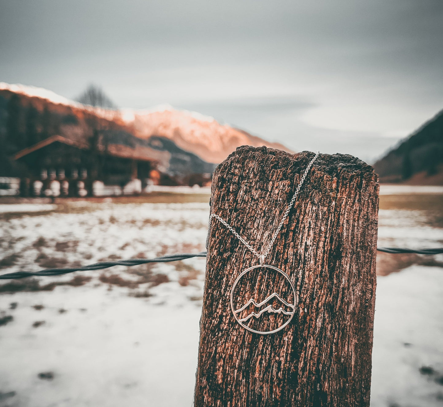 Sterling silver Coastal Mountain Circle Necklace hung on wood fence post with mountain in background