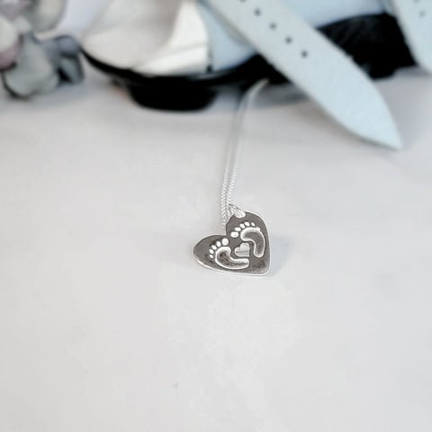 sterling silver, two beautiful curled feet and heart cut out on a heart shaped silver pendant.