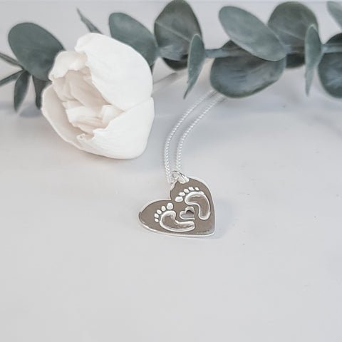 Sterling silver, two beautiful curled feet and heart cut out on a heart shaped silver pendant.