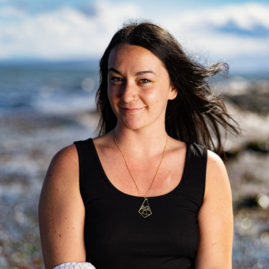 model wearing Geo Mountain design pendant necklace with beach blur background