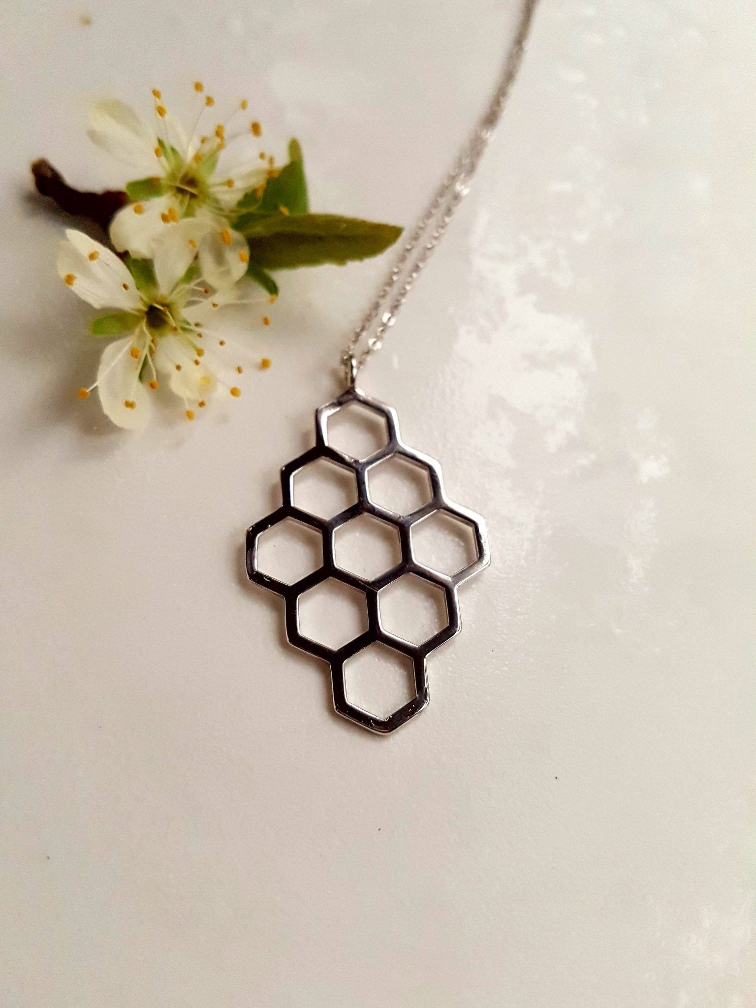 sterling silver honeycomb diamond-shaped pendant necklace with white background and flowers
