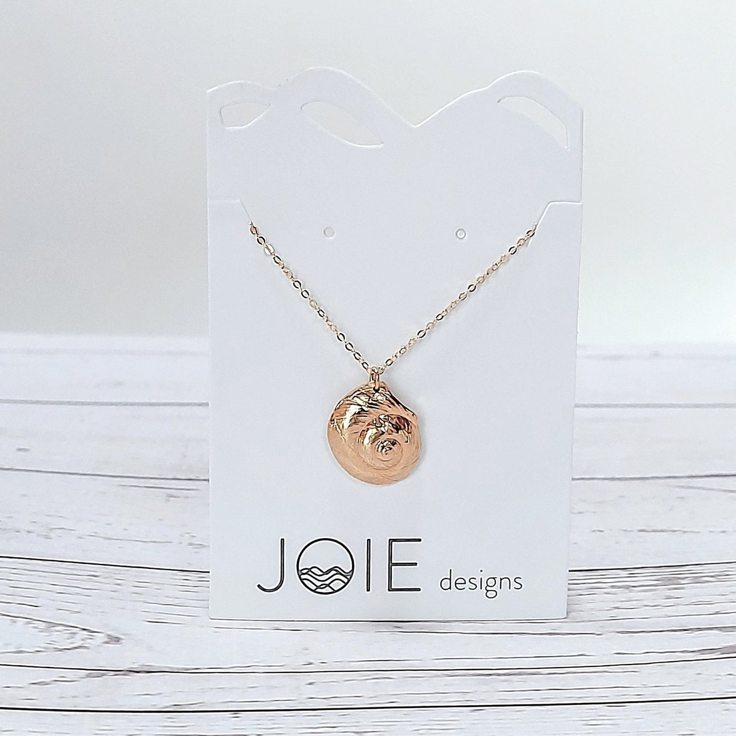 18k plated gold Luna moon snail seashell necklace on a white jewelry card on wood surface, ocean inspired jewelry