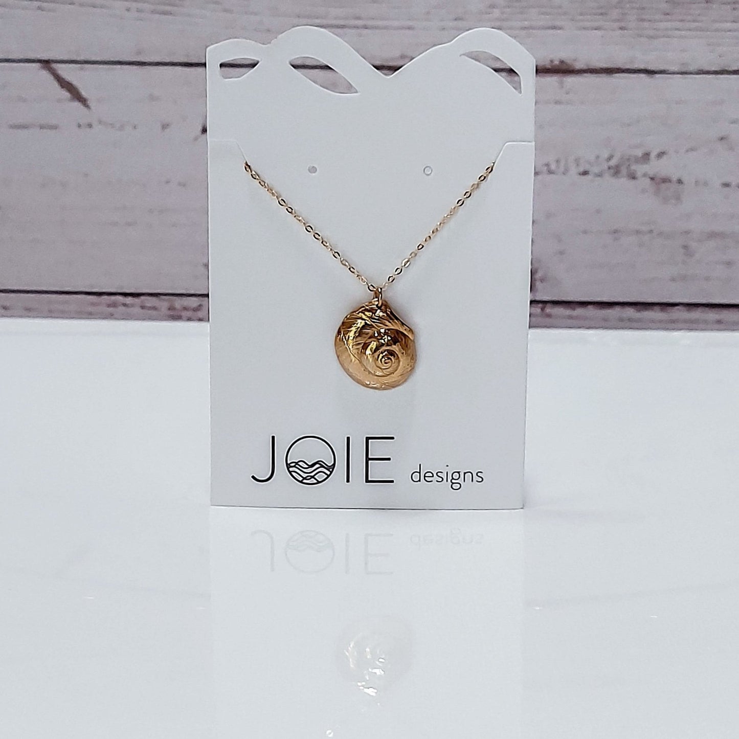 18k plated gold Luna moon snail seashell necklace on a white jewelry card with wood background, ocean jewelry
