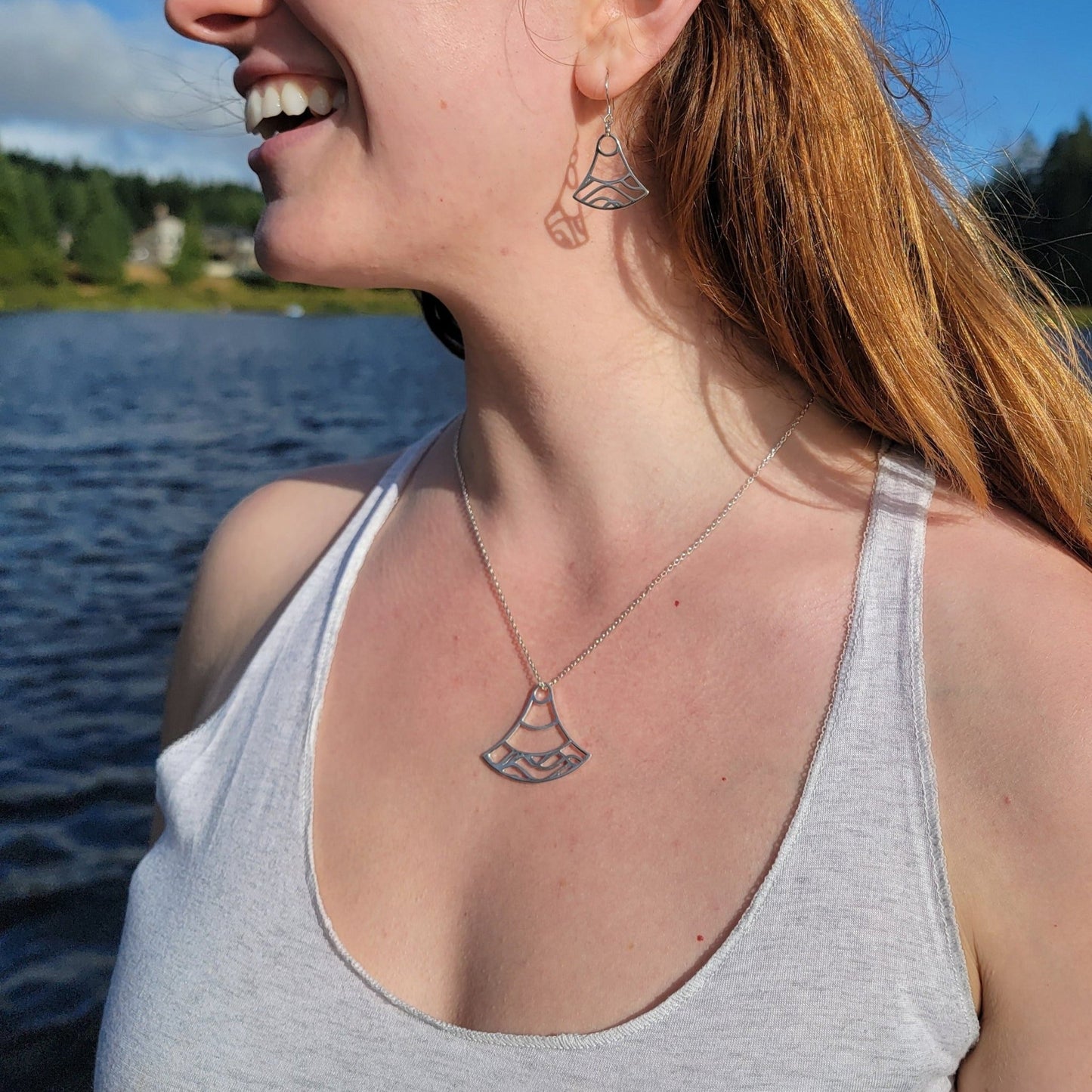 close up of model at lake wearing sterling silver double wave ocean necklace and earrings