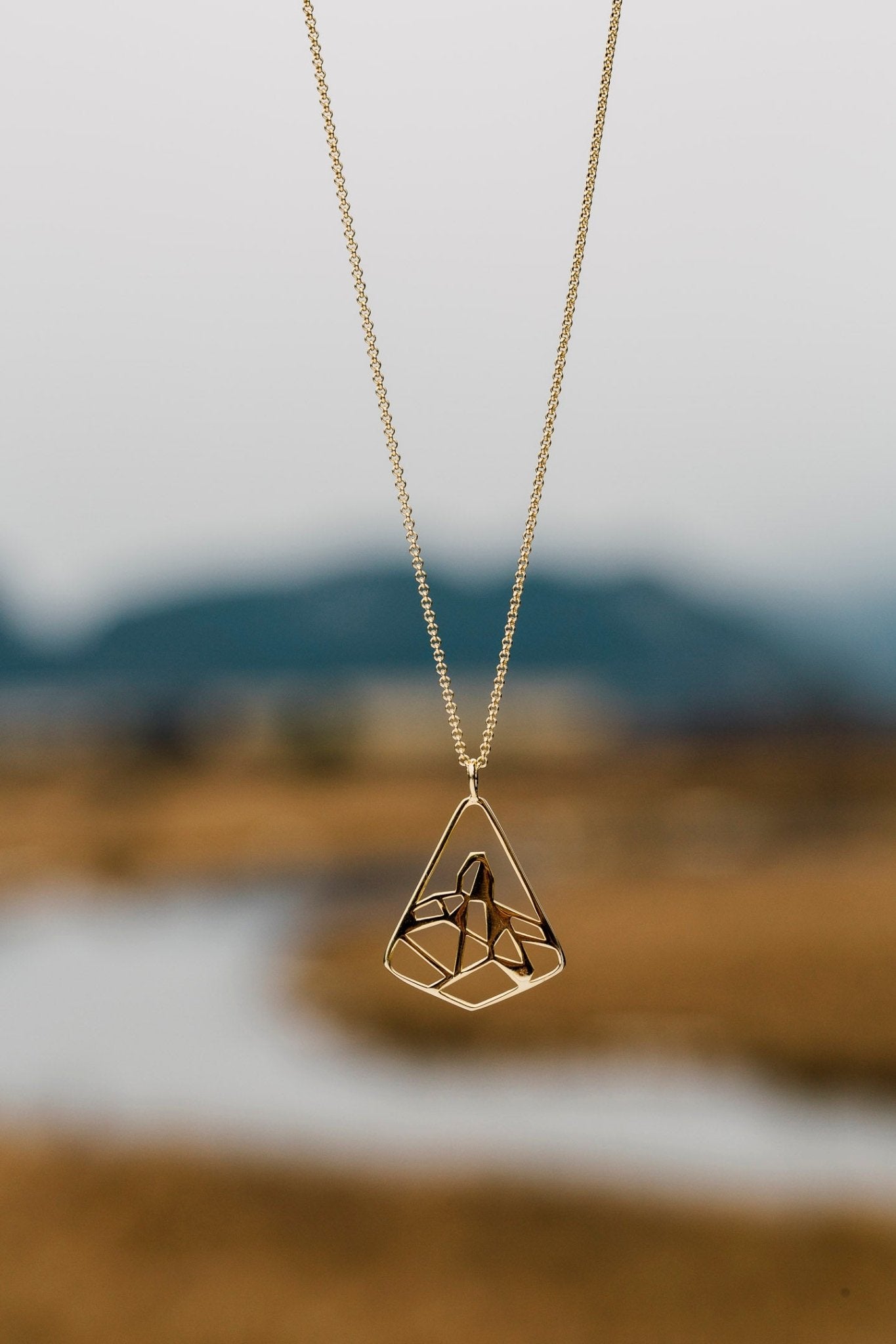 Gold Black Tusk pendant necklace shown against blurred river background
