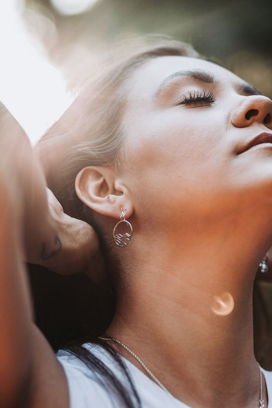 circle earrings, model leaning back to the sunlight wearing sterling silver petite high tide circle design dangle earrings