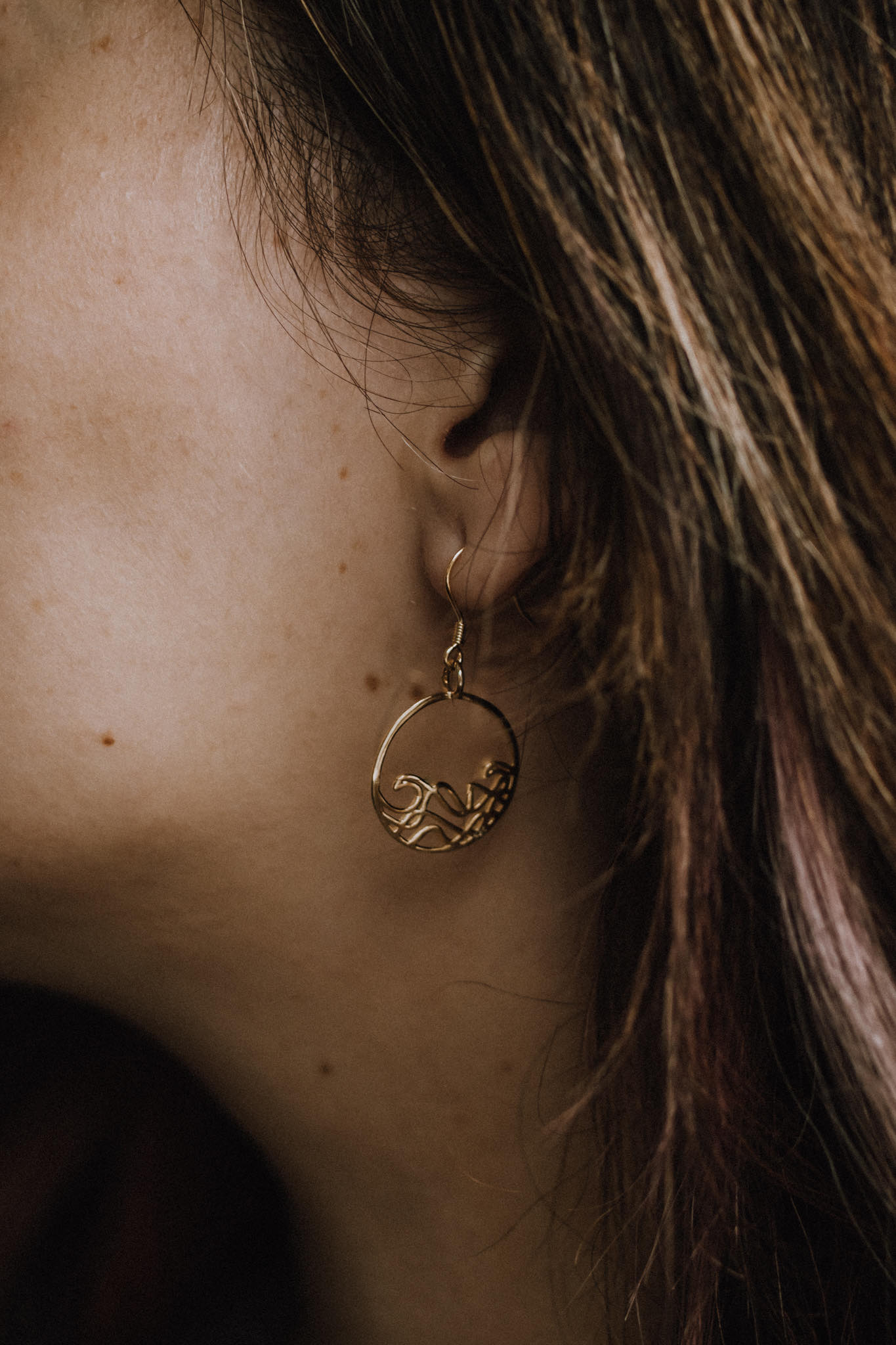 Close up of model wearing 18k plated rose gold plated 925 sterling silver Petite Sombrio circle wave earrings, ocean jewelry