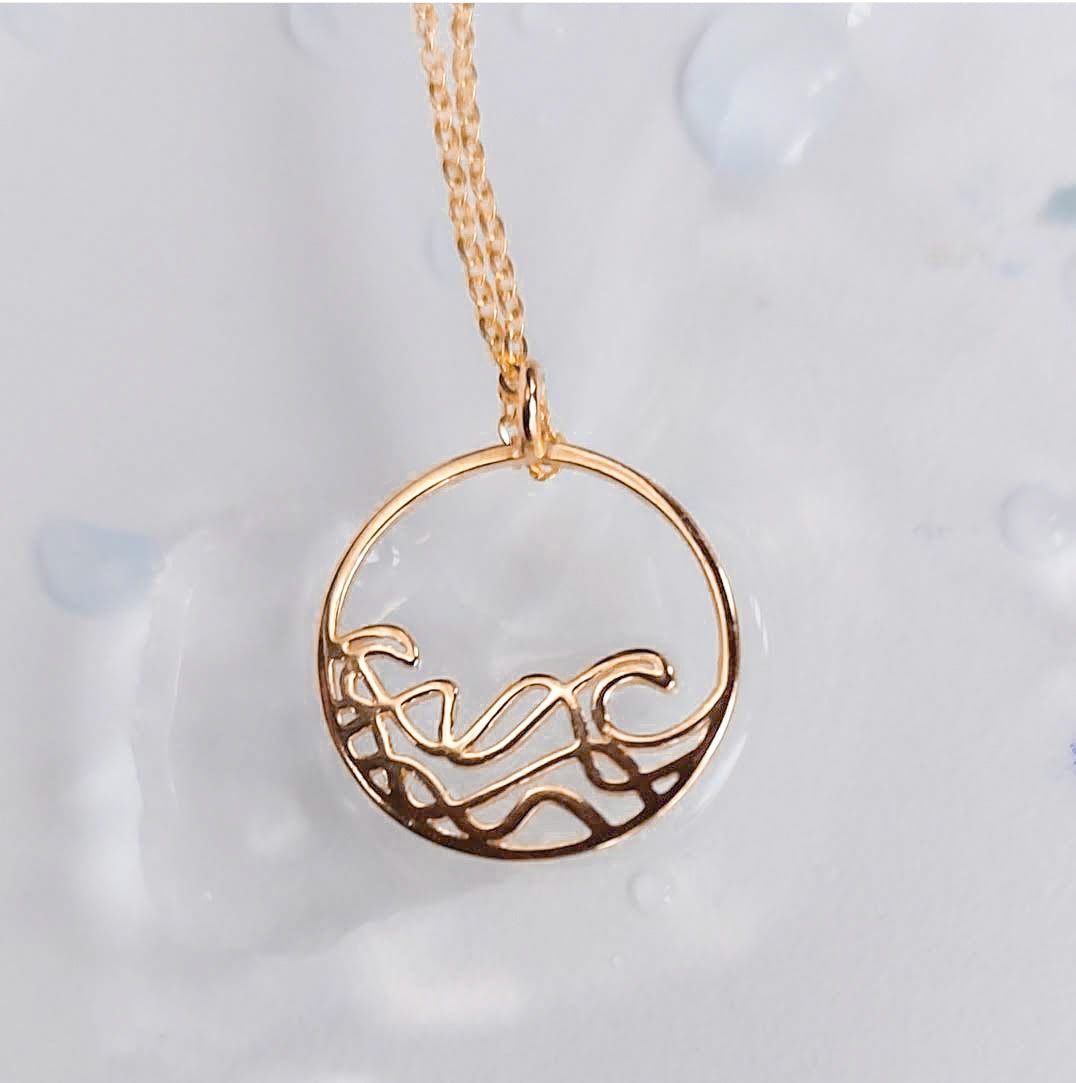 18k gold plated Petite Sombrio Ocean Surf Circle Necklace on a blur background, wave necklace, surf necklace