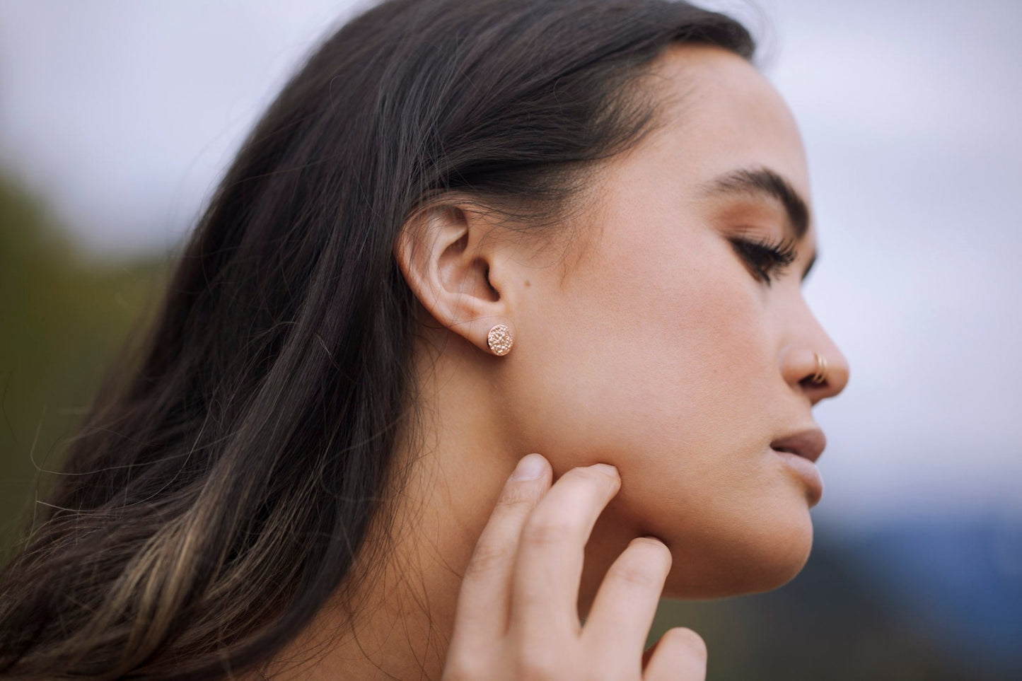 Model wearing 18k rose gold sparkly small circle stud earrings and nature background, ocean inspired jewelry