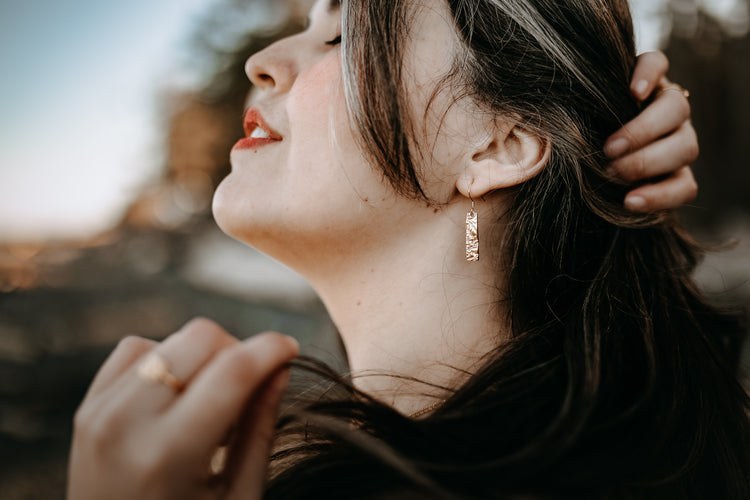 Model wearing gold driftwood textured necklace and earrings and holding a champagne glass