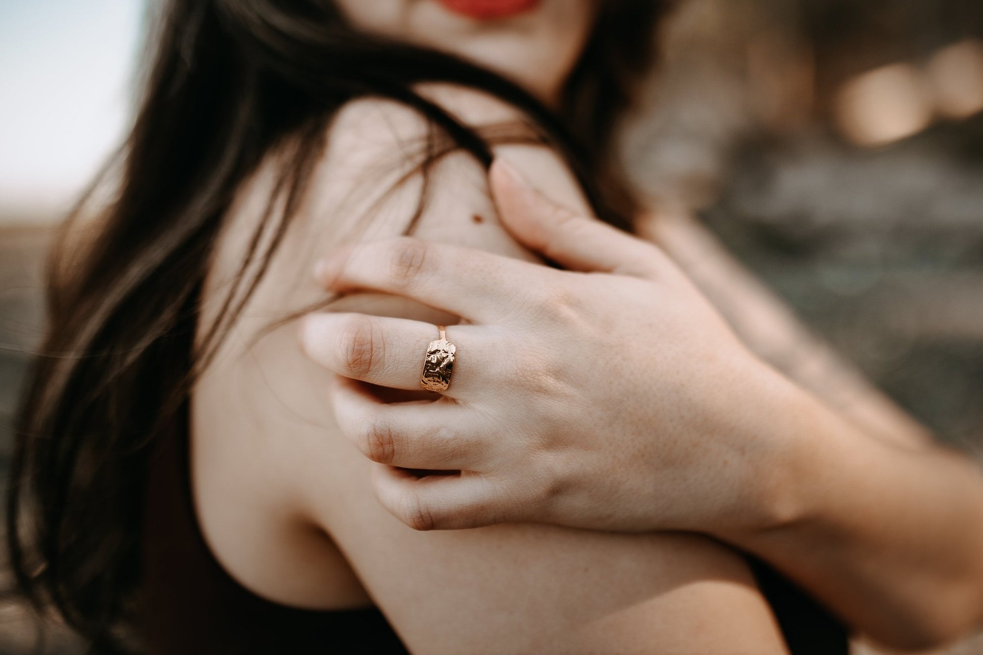 close up of model at the beach wearing gold ring with natural wood textures.