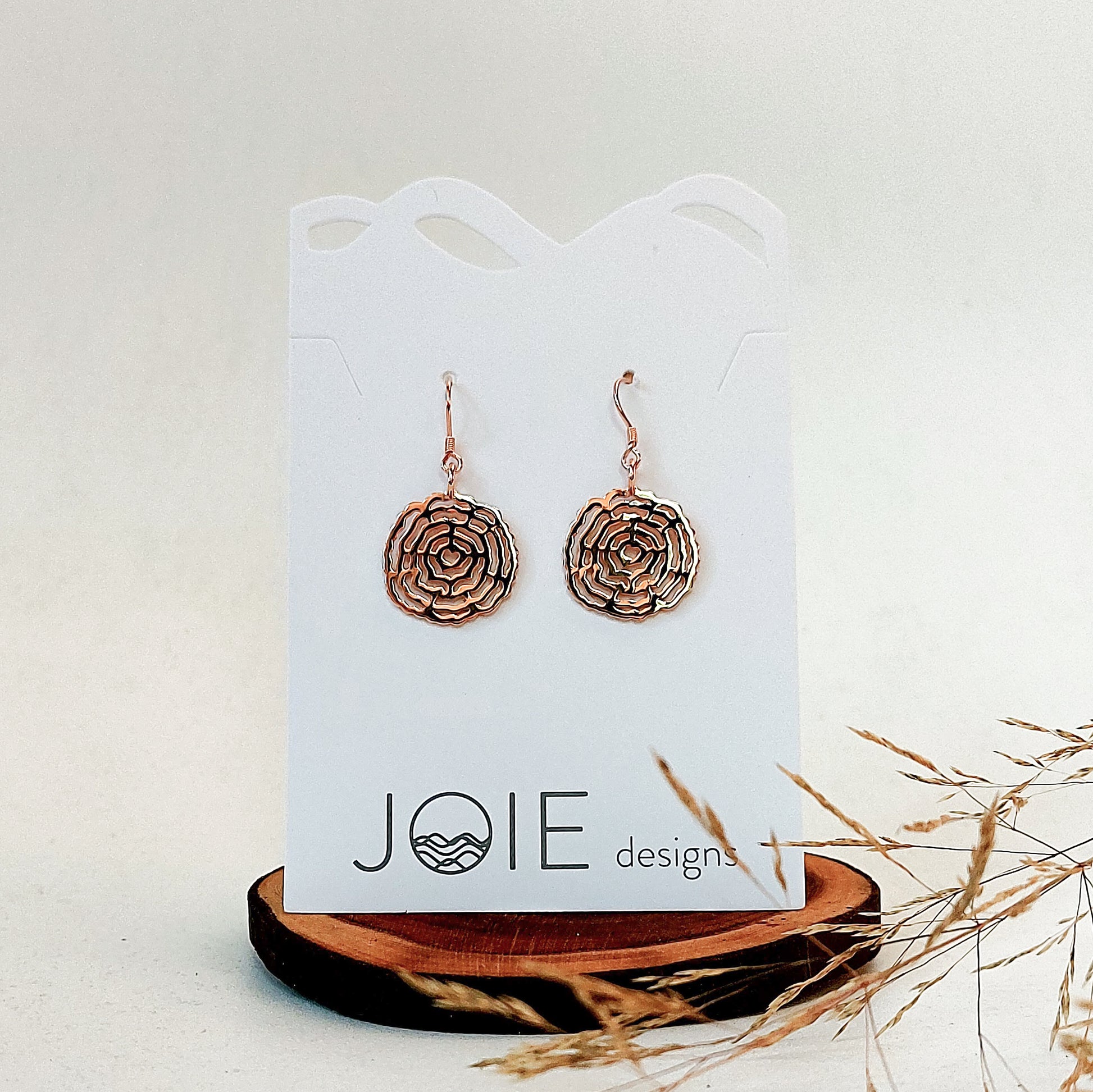 18k plated rose gold circle tree ring dangle earrings on white jewelry card sitting on wood tree ring coaster.