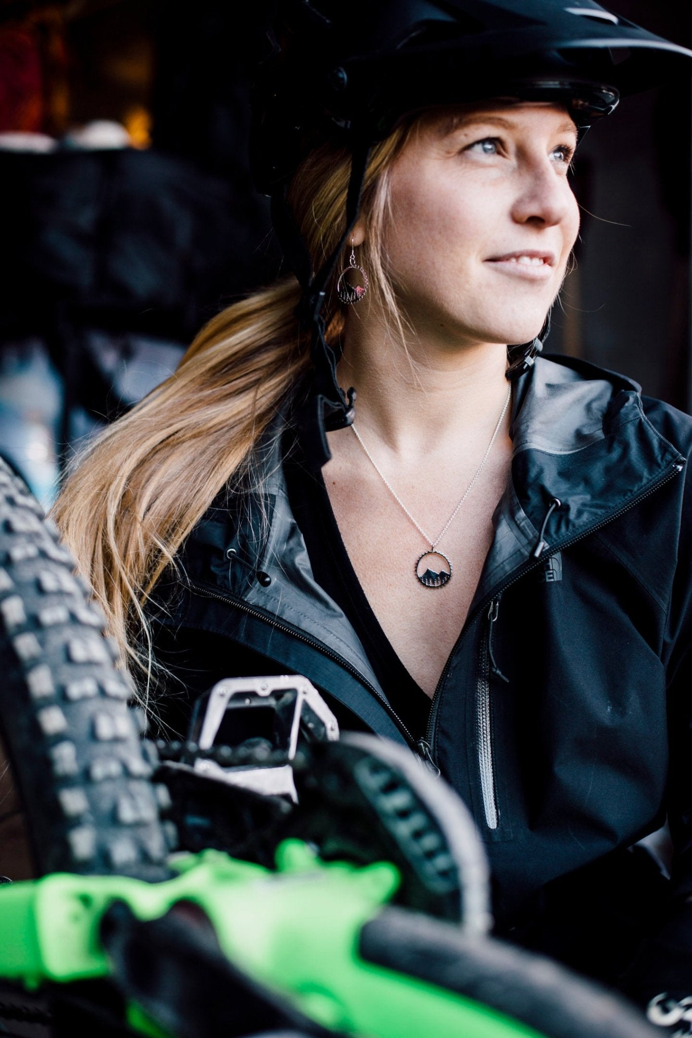Model looking to the right and wearing bike themed necklace with her green bike shown in foreground