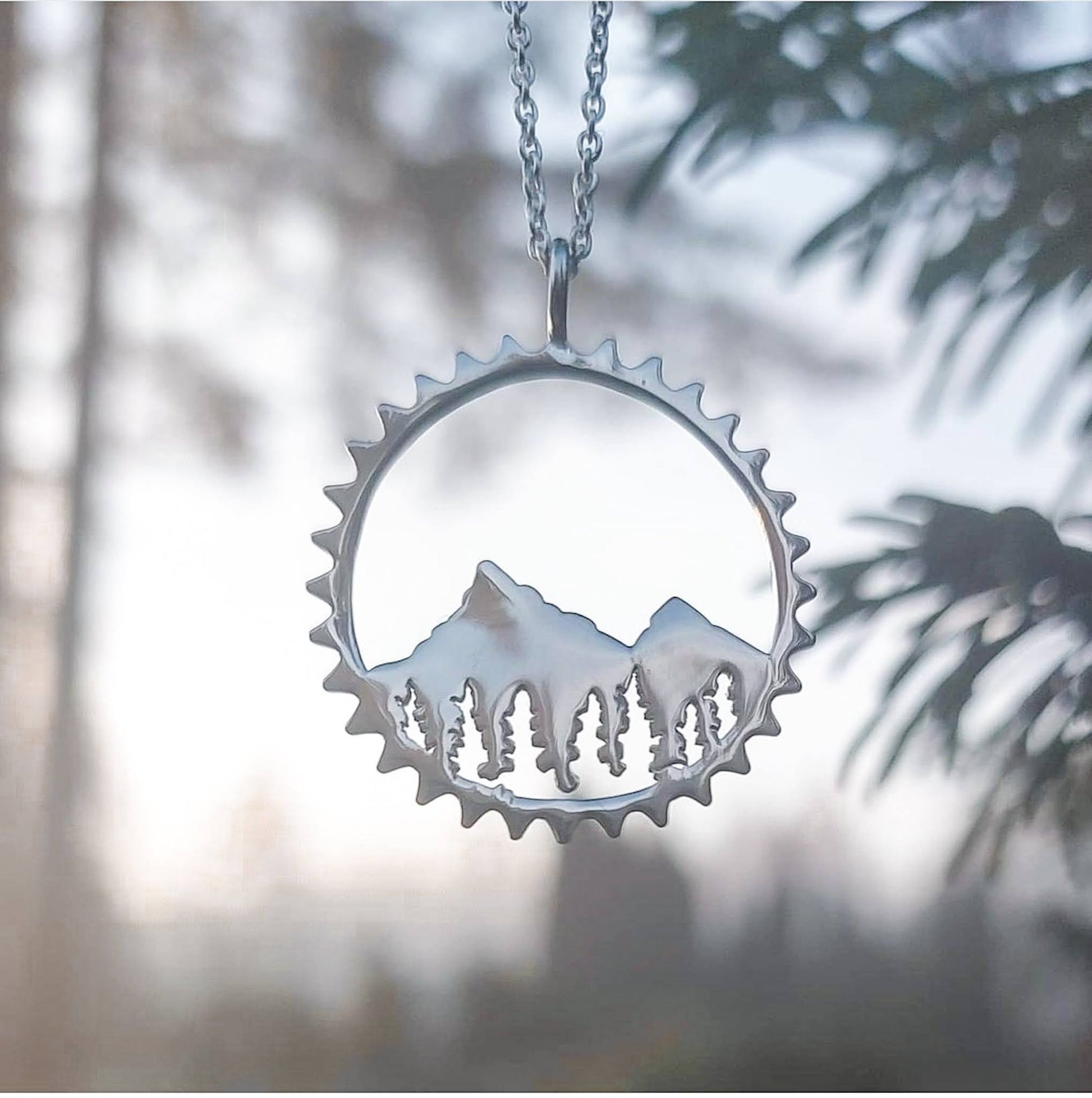 925 sterling silver Amore mountain bike themed pendant shown in front of foggy sunrise with evergreen trees