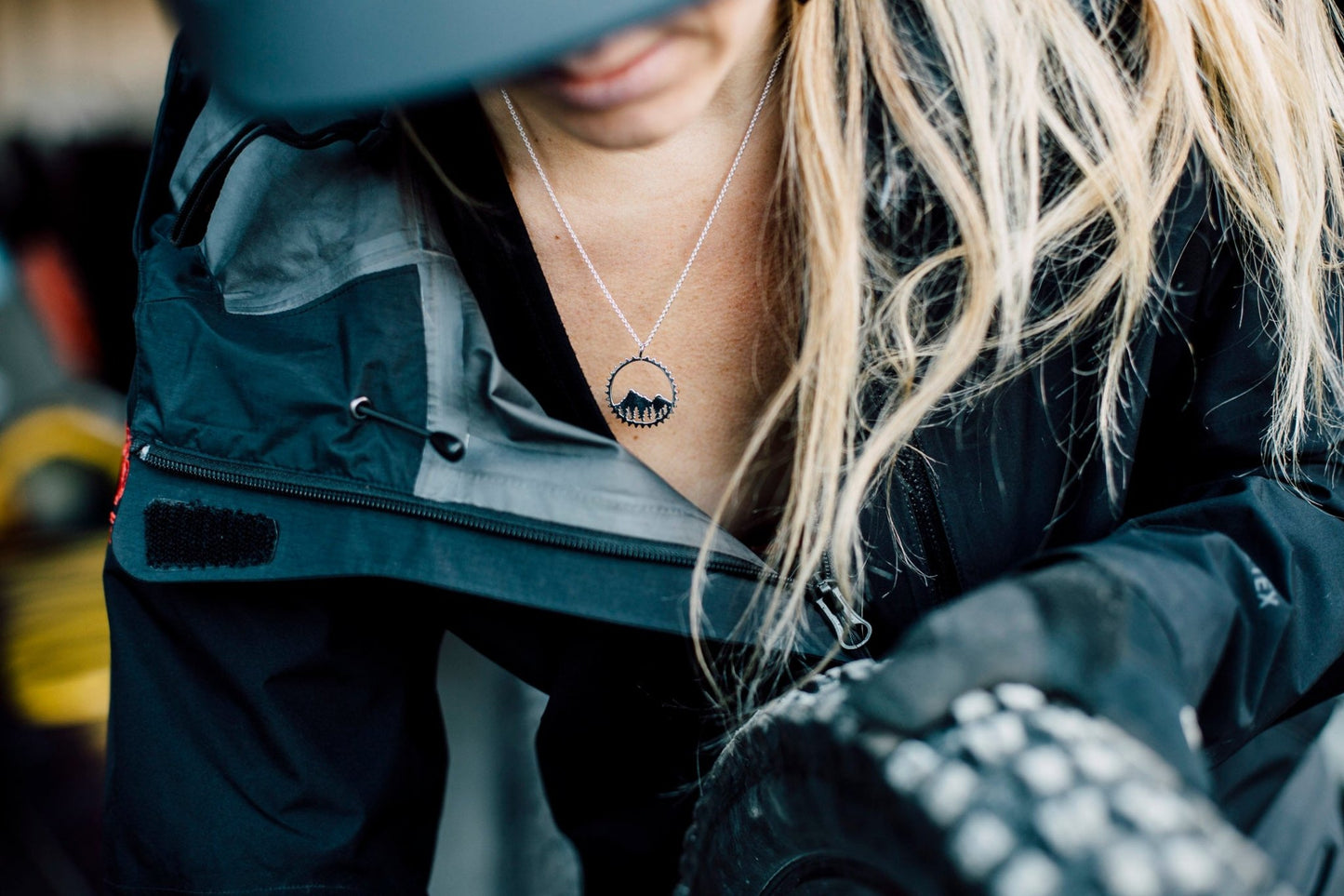 Model wearing silver Amore necklace while wearing black hat and jacket while working on her bike with bike tire in her hand