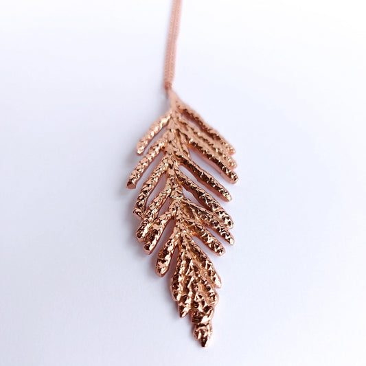 Natural sterling silver cedar leaf plated in 18k rose gold, on a matching delicate cable chain necklace.