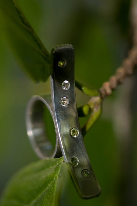 large curved silver statement ring with peridots and cubic zirconia's flush set show on leaf background