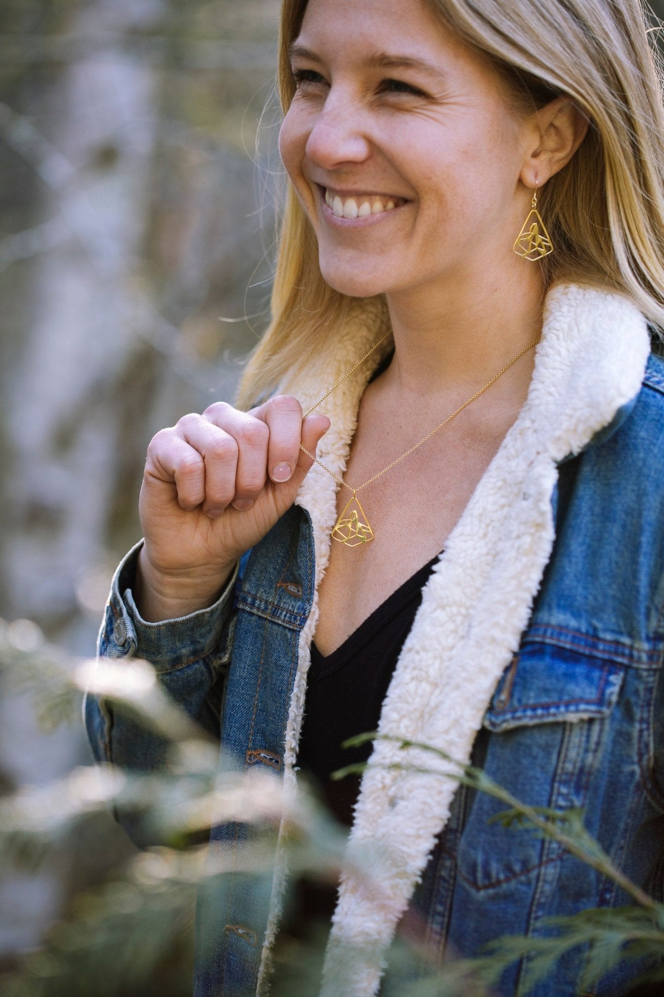 model wearing yellow gold plated black tusk mountain earrings and holding matching gold necklace with blur nature background