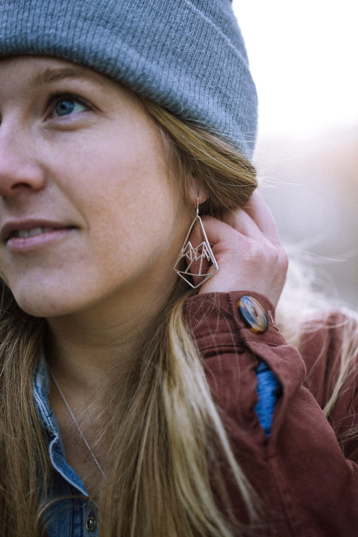 model wearing Geo Mountain design earrings and blue toque with blurred nature background