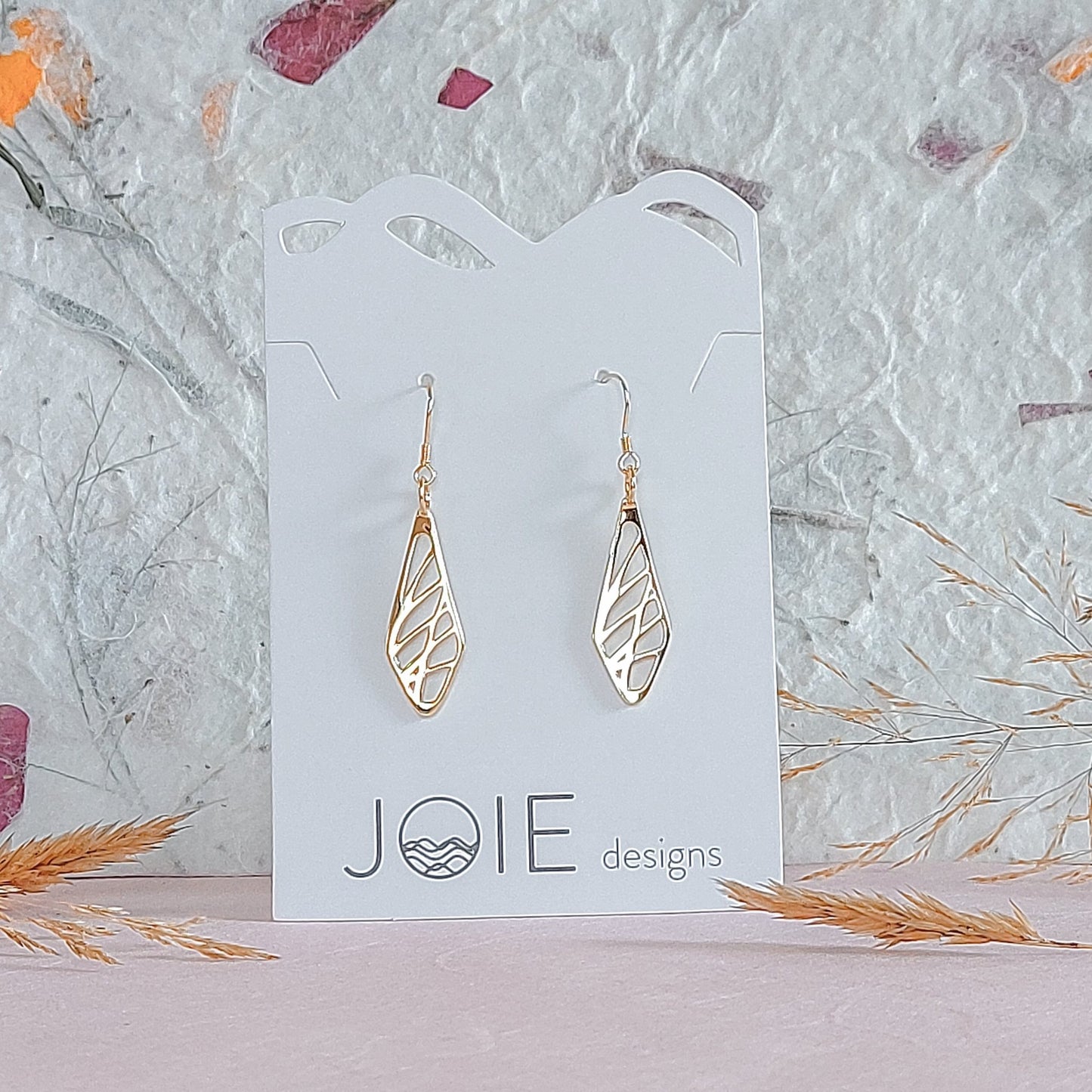 18k plated gold diamond shaped sweet grass earrings on white jewelry card with wildflowers paper background