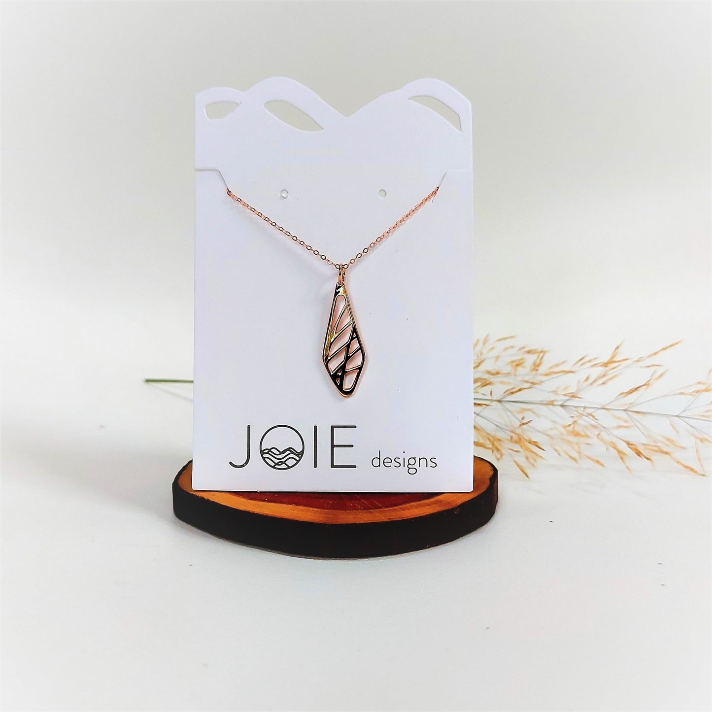 18k plated gold diamond shaped sweet grass necklace on white jewelry card on wood round with dried grass