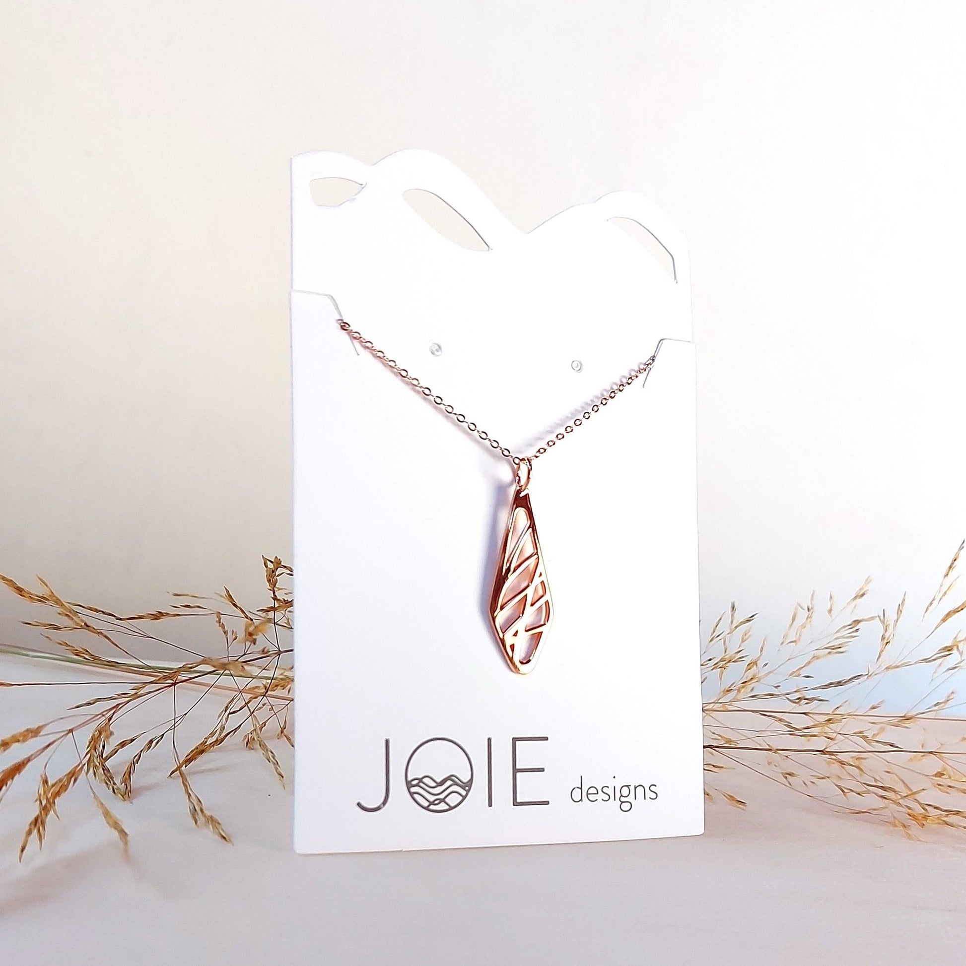 18k plated yellow gold diamond shaped pendant necklace with grass designs shown on jewelry card and dried grass in background
