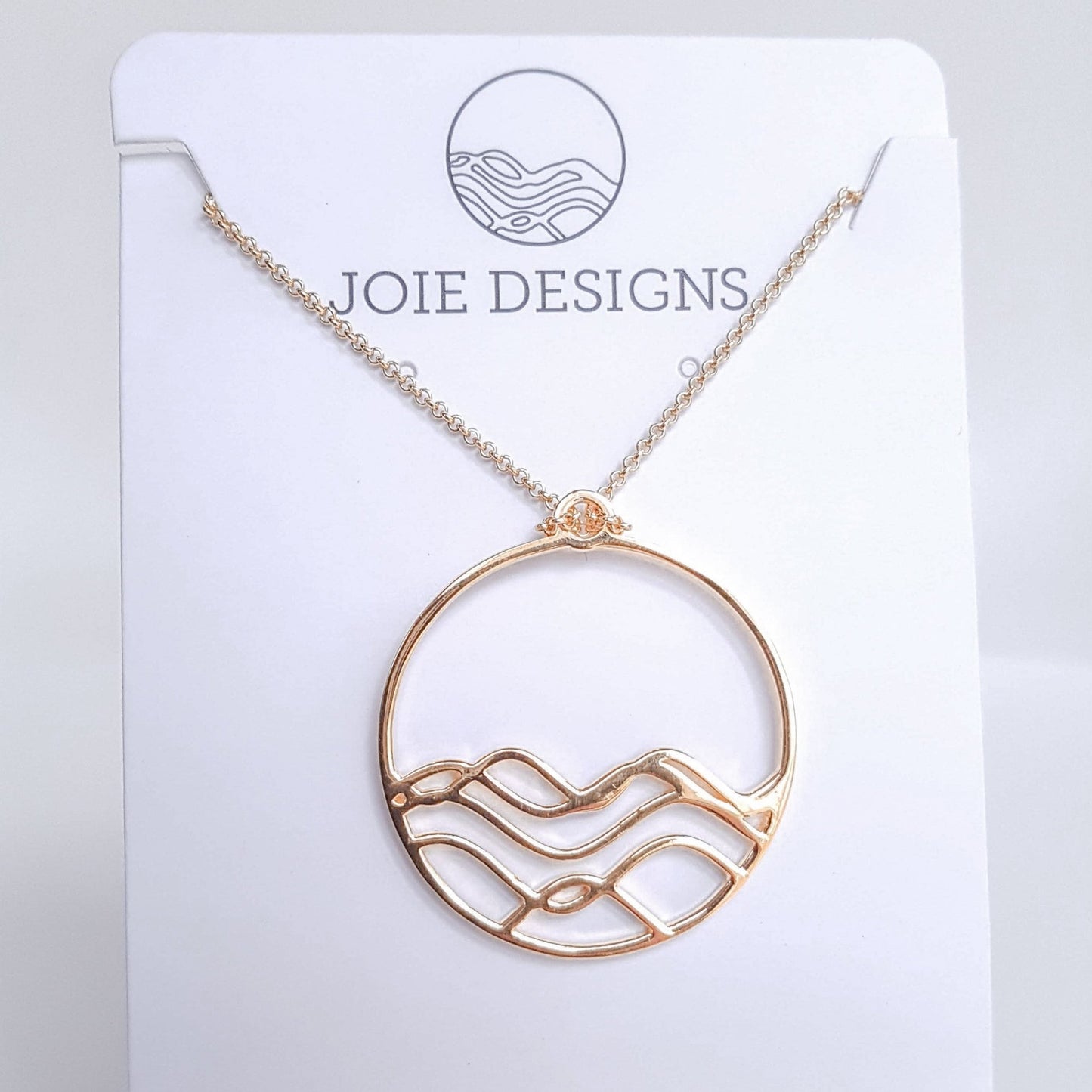 High Tide gold necklace. Circle pendant  filled halfway with wavy lines on a white jewelry card