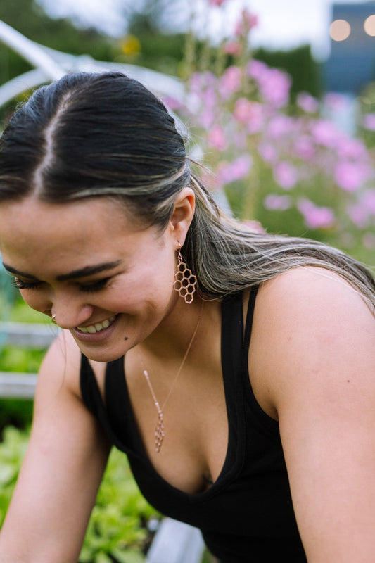 close up of model smiling and wearing sterling silver diamond honeycomb earrings in garden