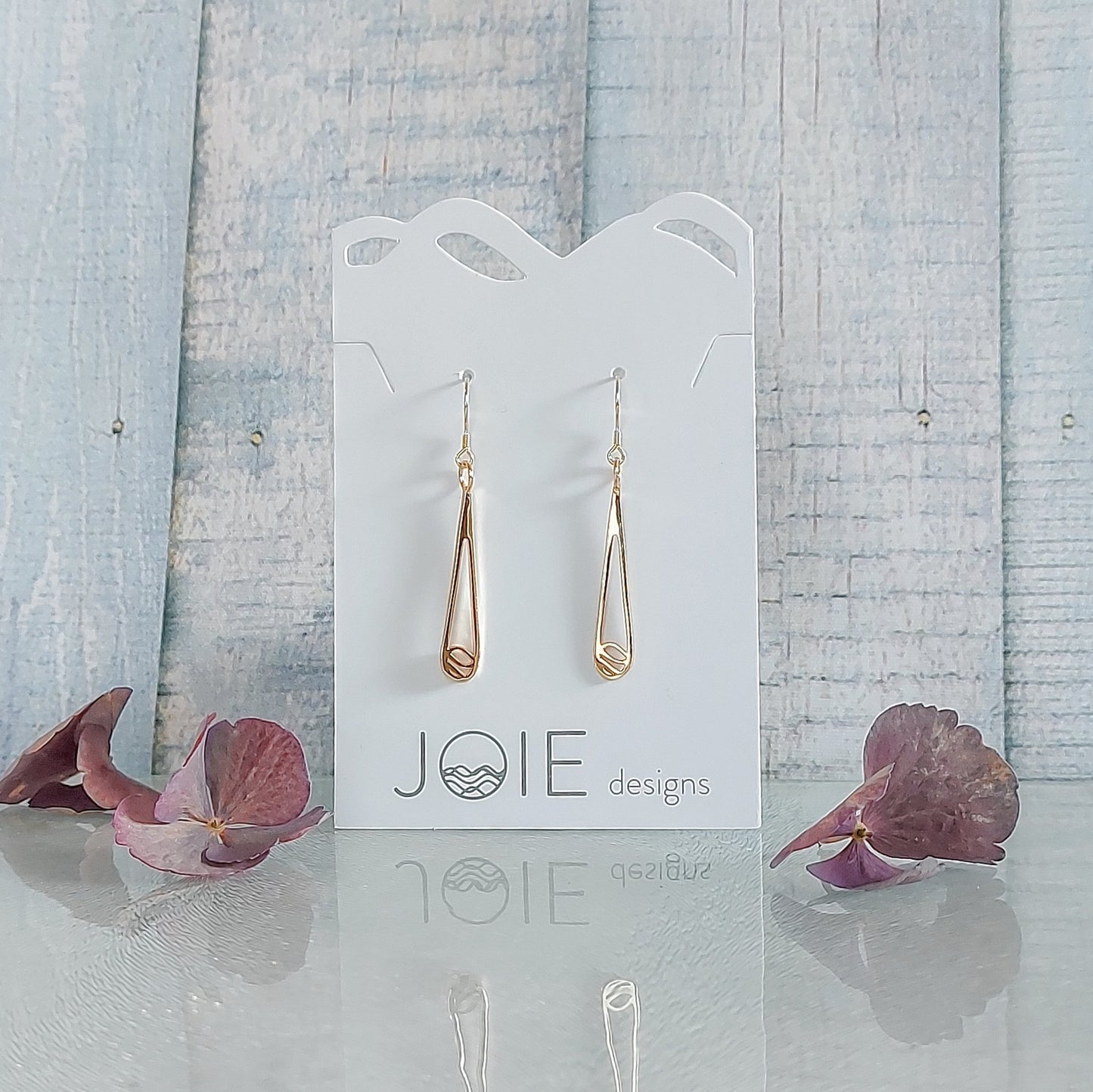 18k yellow gold plated Indra raindrop design earrings showcased on a jewellery card with book background and purple flowers
