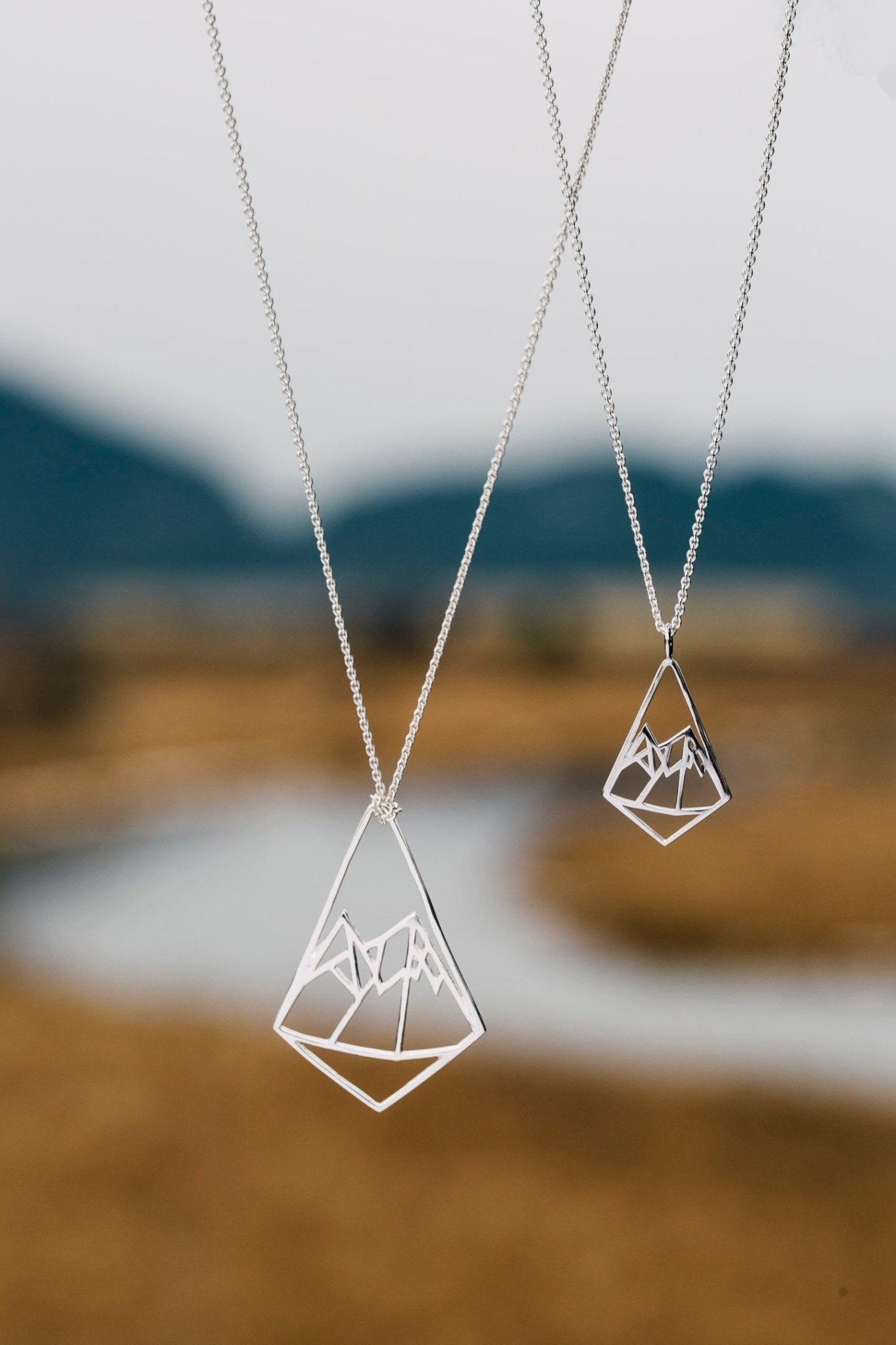 different size diamond shaped pendants on different length necklace chains with river and mountain background