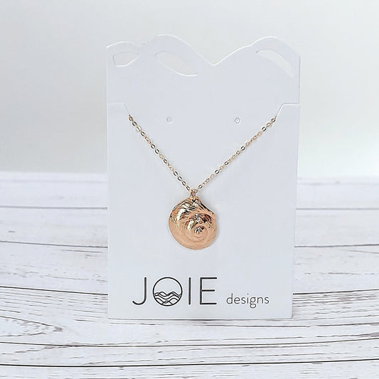 18k plated  gold Luna moon snail seashell necklace on a white jewelry card on wood surface, ocean inspired jewelry