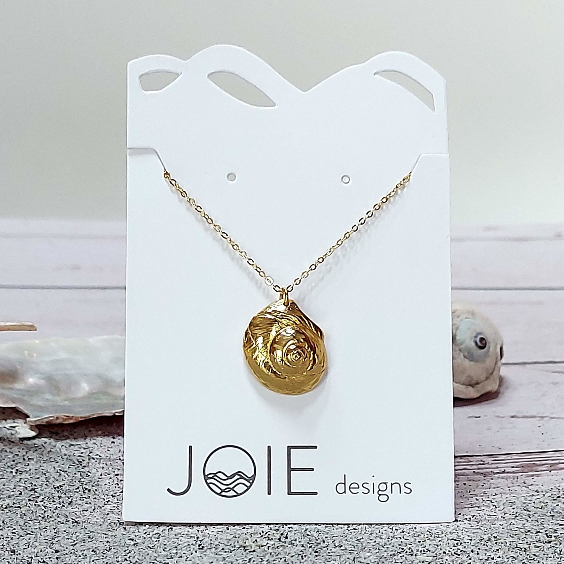 18k plated  gold Luna moon snail seashell necklace on a white jewelry card with sand and shells, ocean inspired jewelry