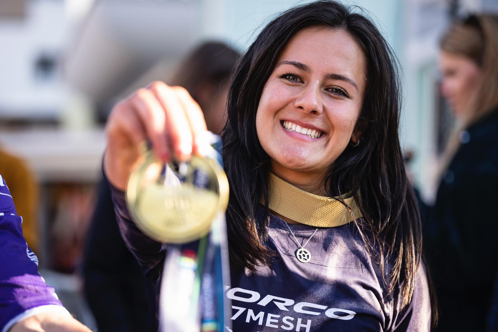 Female athlete holding gold medal and wearing silver bike chain ring necklace