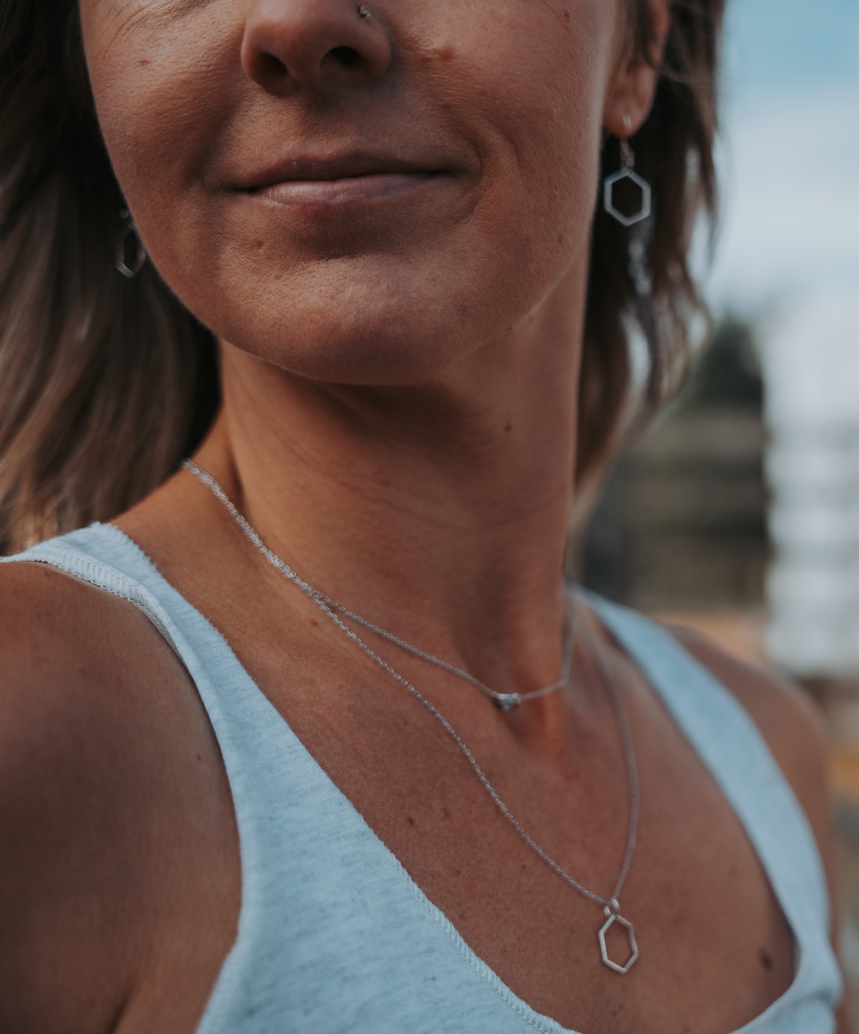 close up of model wearing layered silver Tofino wave and Melina hexagon necklaces 