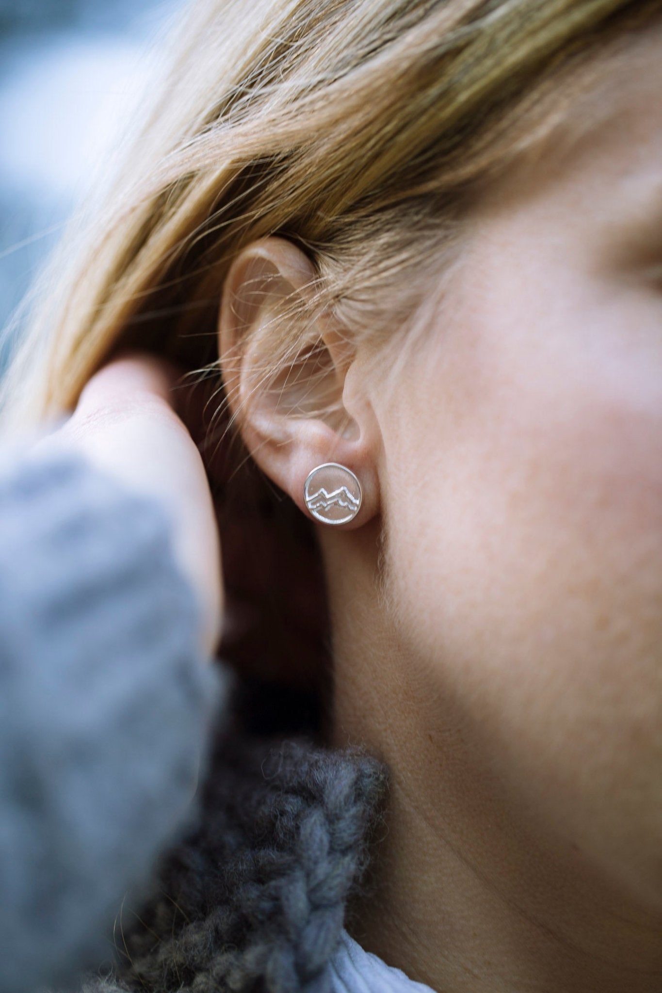 Close up of model wearing small round stud earrings with mountains