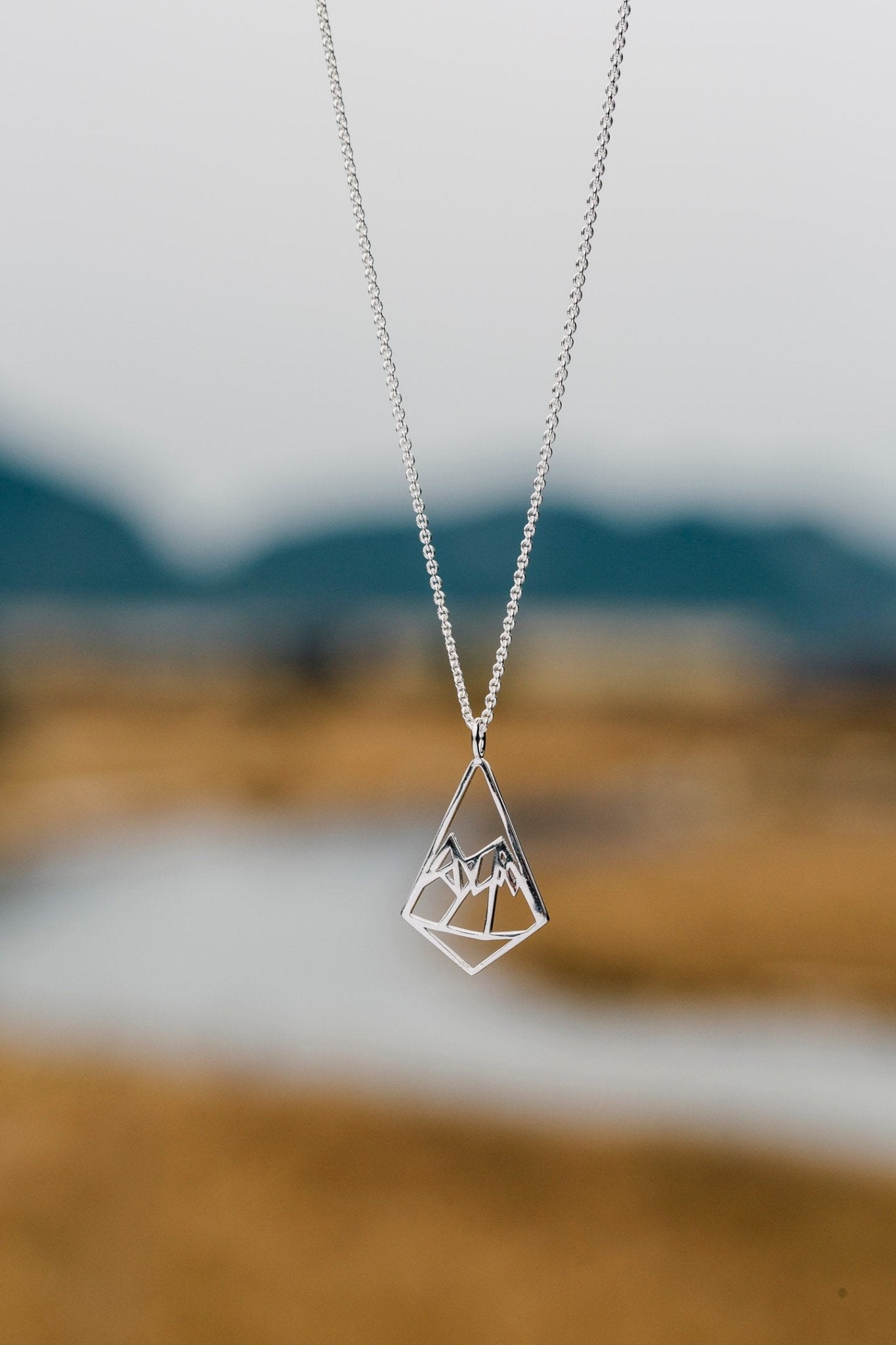 Small Geo Mountain pendant necklaces shown against blurred river background