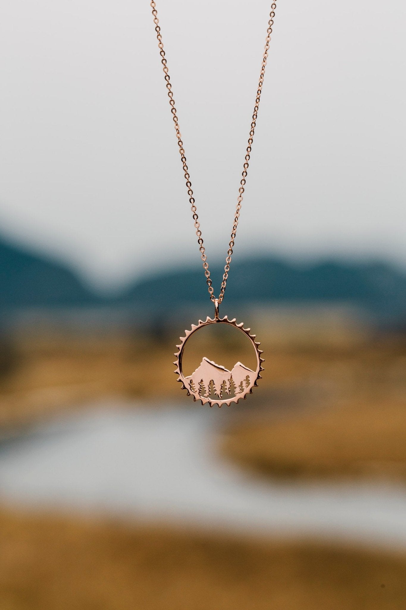 Rose gold Amore pendant necklace shown with blurred blurred river background