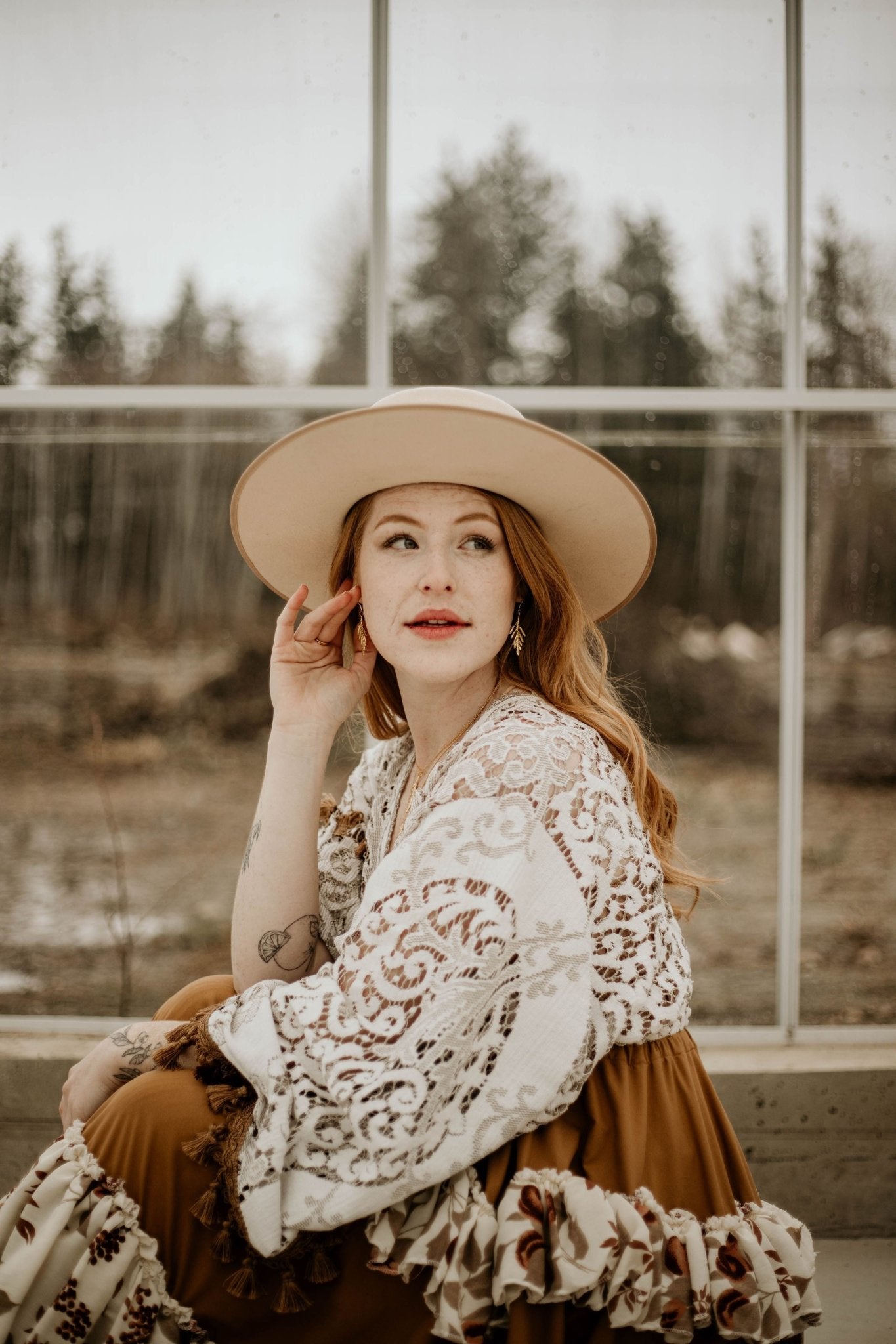 model wearing 18k gold plated cedar leaf design dangle earrings with a hat