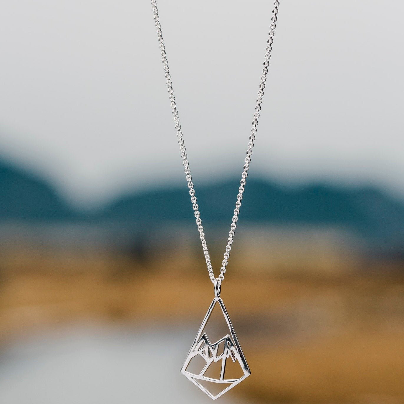 925 sterling silver geometric mountains design pendant necklace on a blur river background
