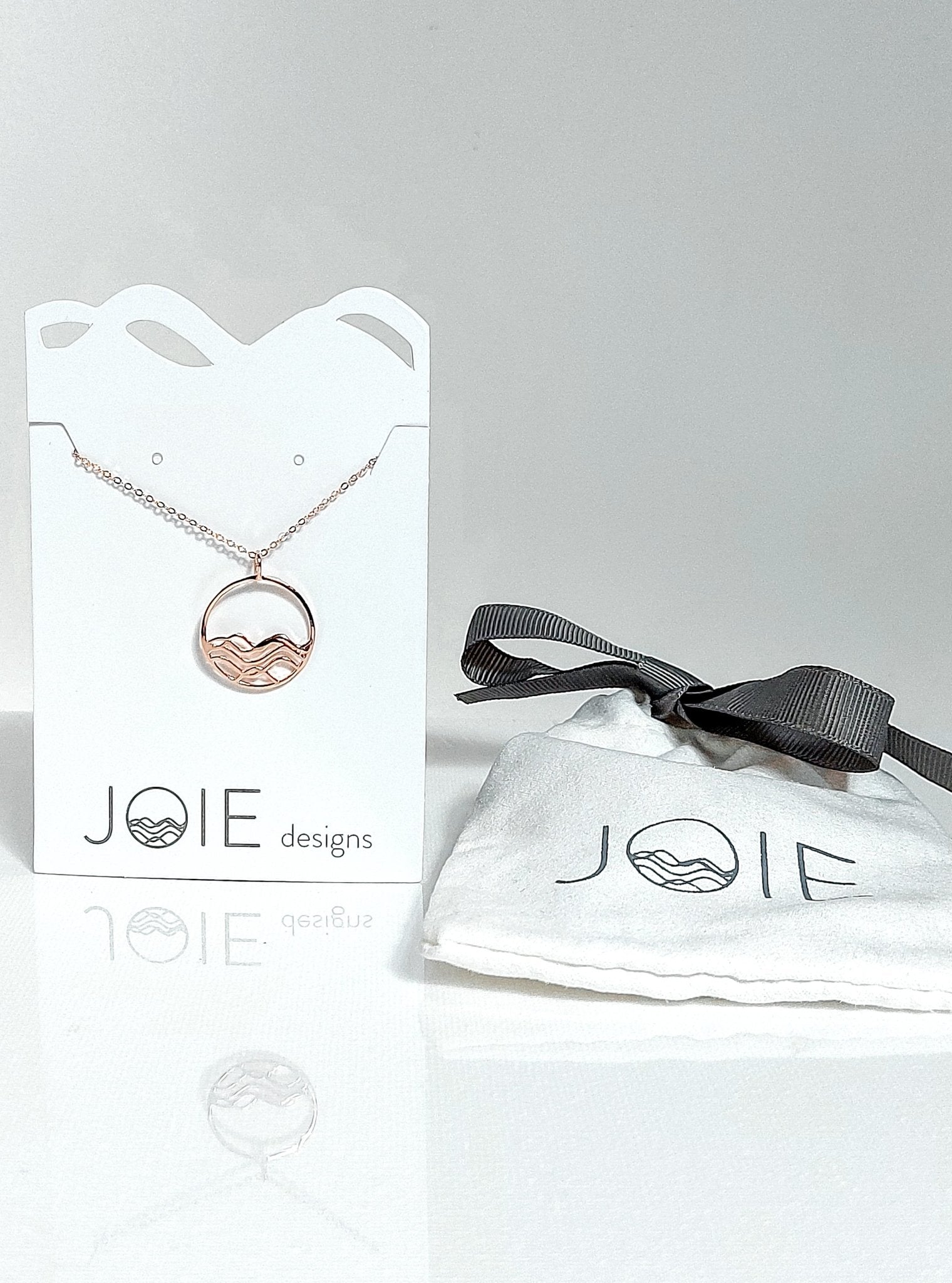 18k rose gold plated petite high tide circle pendant necklace on a white jewelry card with matching faux suede bag.