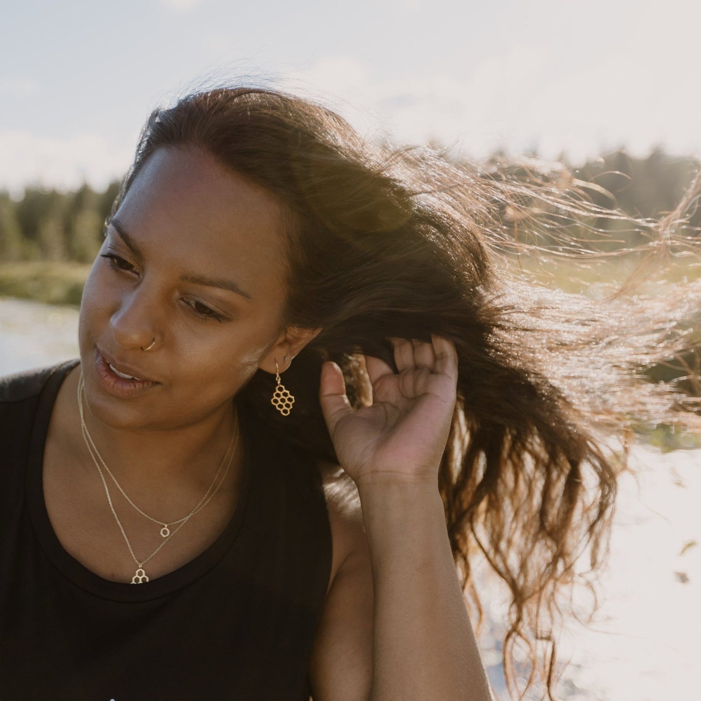 gold honeycomb earrings and necklaces layered on model with wind in her hair